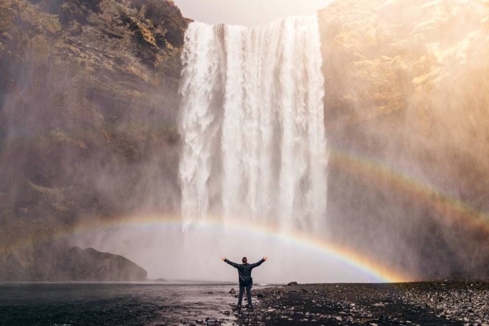 A person standing in front of a waterfall with rainbows.